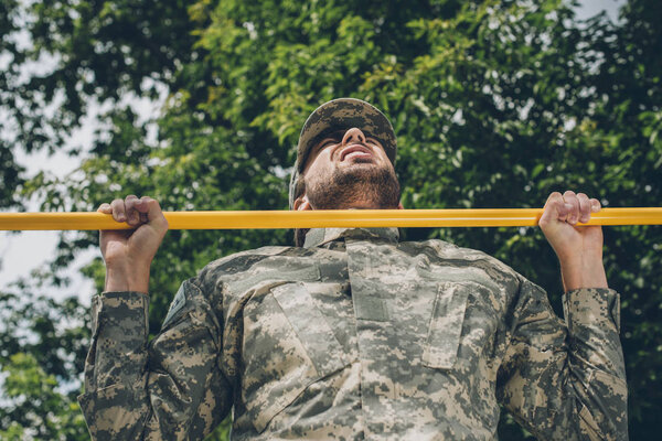 low angle view of soldier in military uniform pulling himself up on crossbar