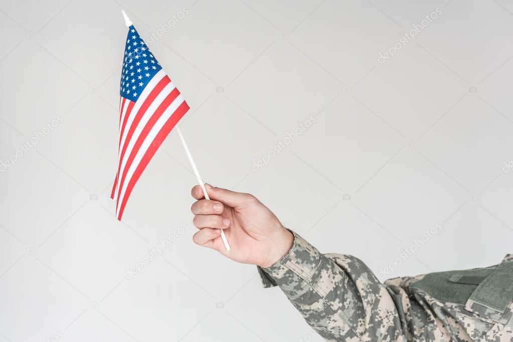 partial view of boy in camouflage clothing holding american flagpole in hand isolated on grey