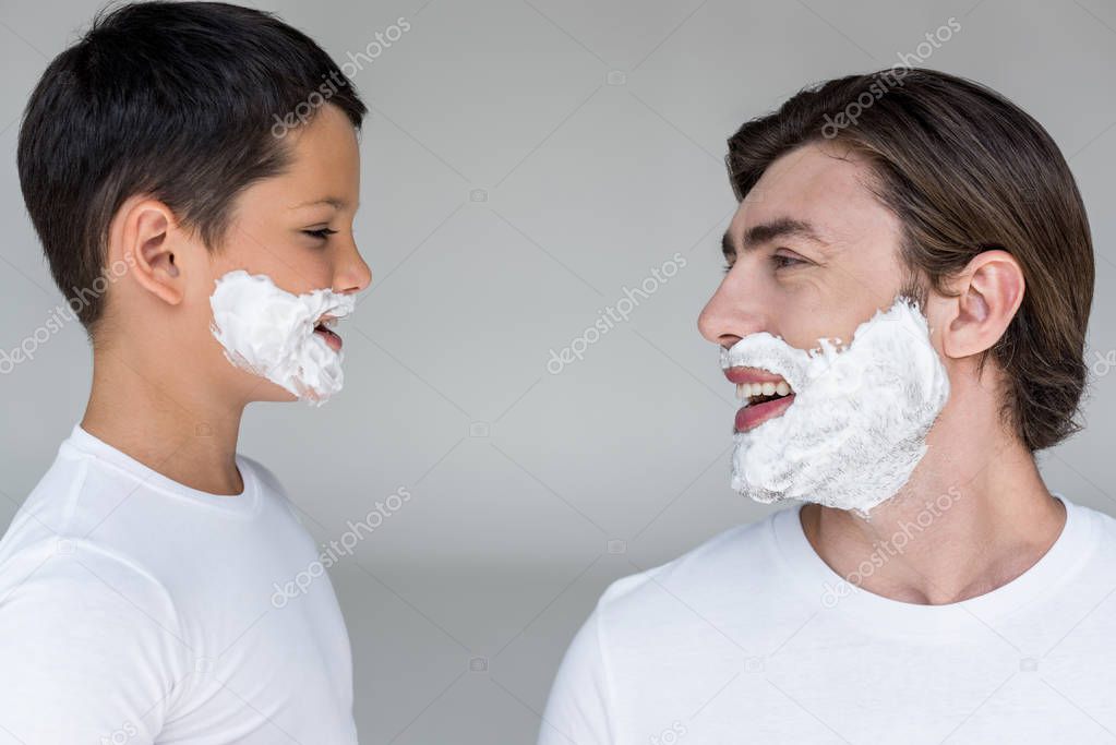 side view of happy father and son with shaving foam on faces on grey background