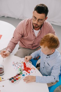 öğretmenin sınıfta masada resim çizmek için küçük çocuk yardım yüksek açılı görünüş