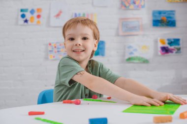 gülümseyen çocuk odasında heykelcilik için renkli hamuru ile masada oturan portresi