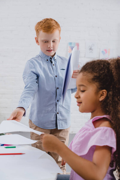 selective focus of multicultural preschoolers with papers in classroom