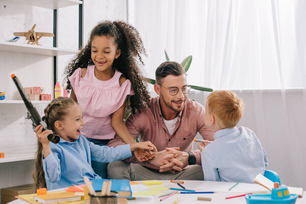 smiling teacher in eyeglasses and cheerful interracial kids in classroom