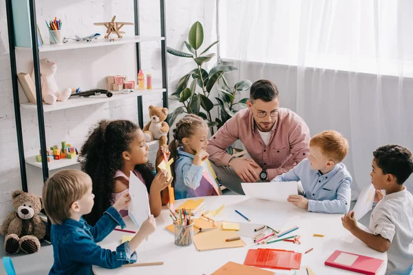 先生と塗料 教室で紙とテーブルで異人種間の幼児 — ストック写真