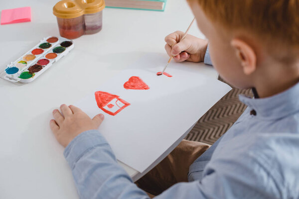 partial view of preschooler red hair boy drawing picture at table in classroom