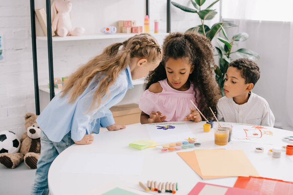 multiethnic preschoolers looking at african american classmate drawing picture at table in classroom