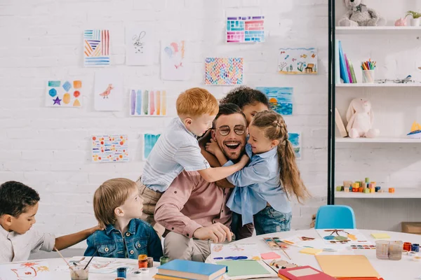 Międzyrasowe Dzieci Przytulanie Szczęśliwy Nauczyciel Tabeli Klasie — Zdjęcie stockowe