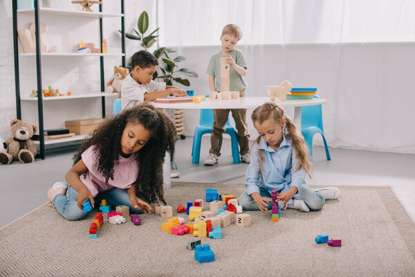 focused multiracial preschoolers playing with wooden blocks in classroom