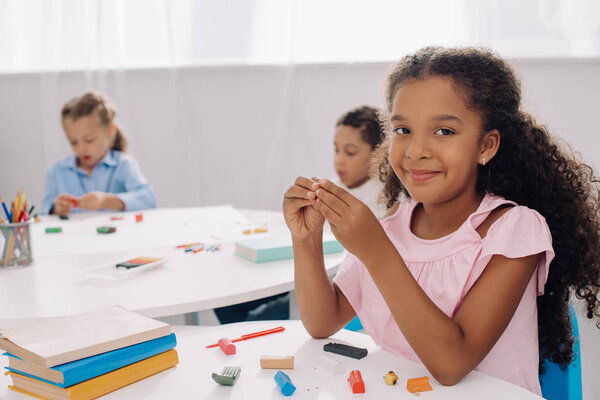 selective focus of smiling african american kid with plasticine in classroom