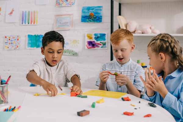 portrait of cute multiethnic preschoolers sculpturing figures with plasticine in classroom
