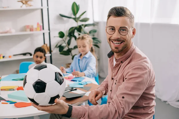 Profesor Sonriente Con Pelota Fútbol Compañeros Clase Multiculturales Detrás Aula — Foto de Stock