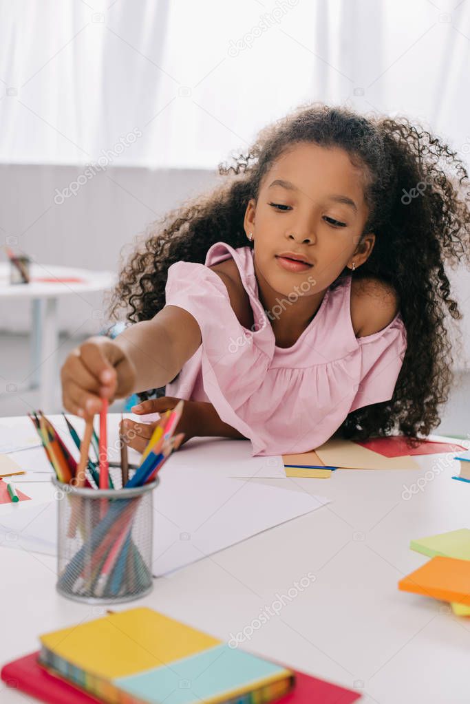portrait of african american kid taking pencil while drawing colorful picture at table