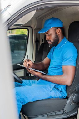african american delivery man writing something to clipboard in van clipart