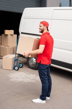 karton kutu ayakta beyaz minibüsü sokakta yakınındaki ile üniformalı genç teslimatçı yan görünüm