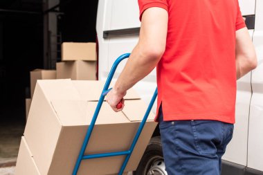 cropped shot of delivery man with cardboard boxes on delivery cart clipart