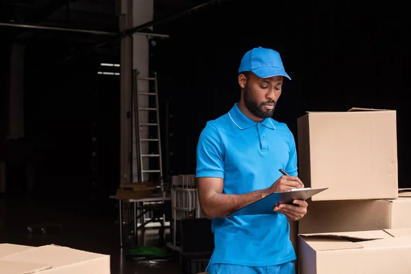 Africano Americano Repartidor Escribir Algo Portapapeles Cerca Cajas — Foto de Stock