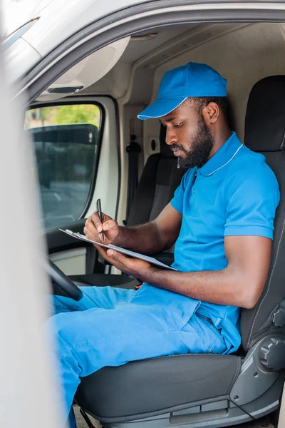 african american delivery man writing something to clipboard in van