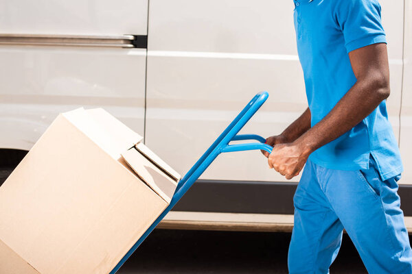 cropped image of african american delivery man with cart and boxes