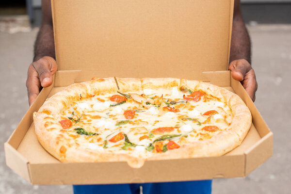 cropped image of african american delivery man showing pizza