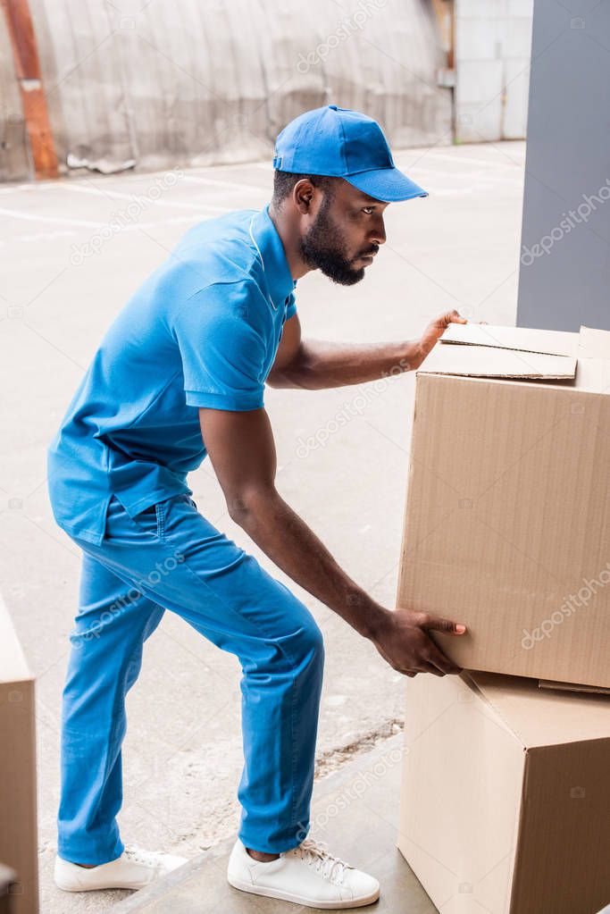 side view of african american delivery man putting boxes on pile