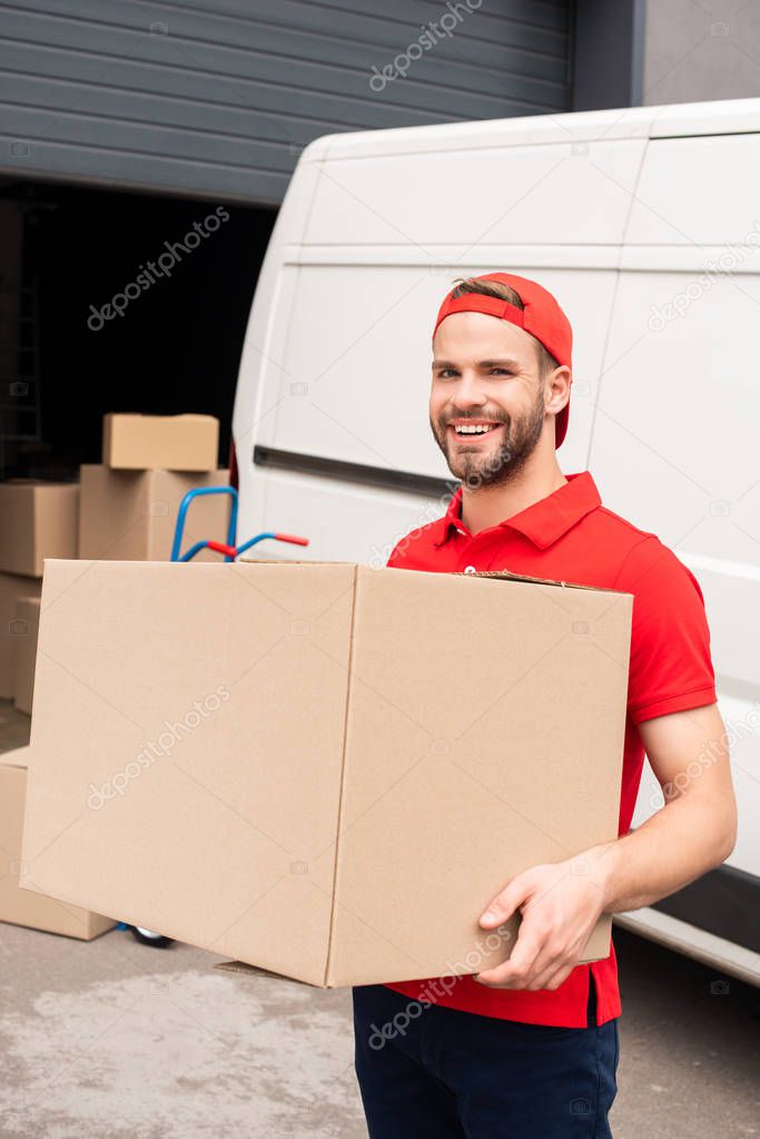 portrait of smiling delivery man in uniform holding cardboard box