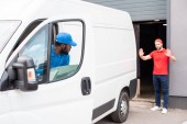 multiethnic delivery men in uniform parking white van on street