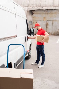 karton kutu ayakta beyaz minibüsü sokakta yakınındaki ile üniformalı genç teslimatçı yan görünüm