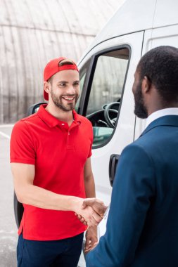 smiling delivery man and african american businessman shaking hands clipart