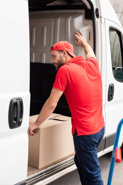 young delivery man in red uniform standing near van with cargo