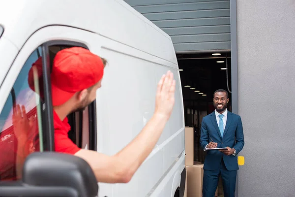 Чоловік Доставки Фургоні Махає Усміхненим Афроамериканським Бізнесменом Блокнотом — стокове фото
