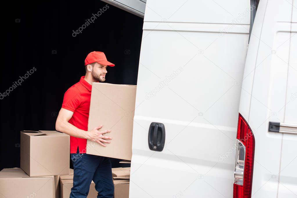 side view of young delivery man discharging cardboard boxes from van