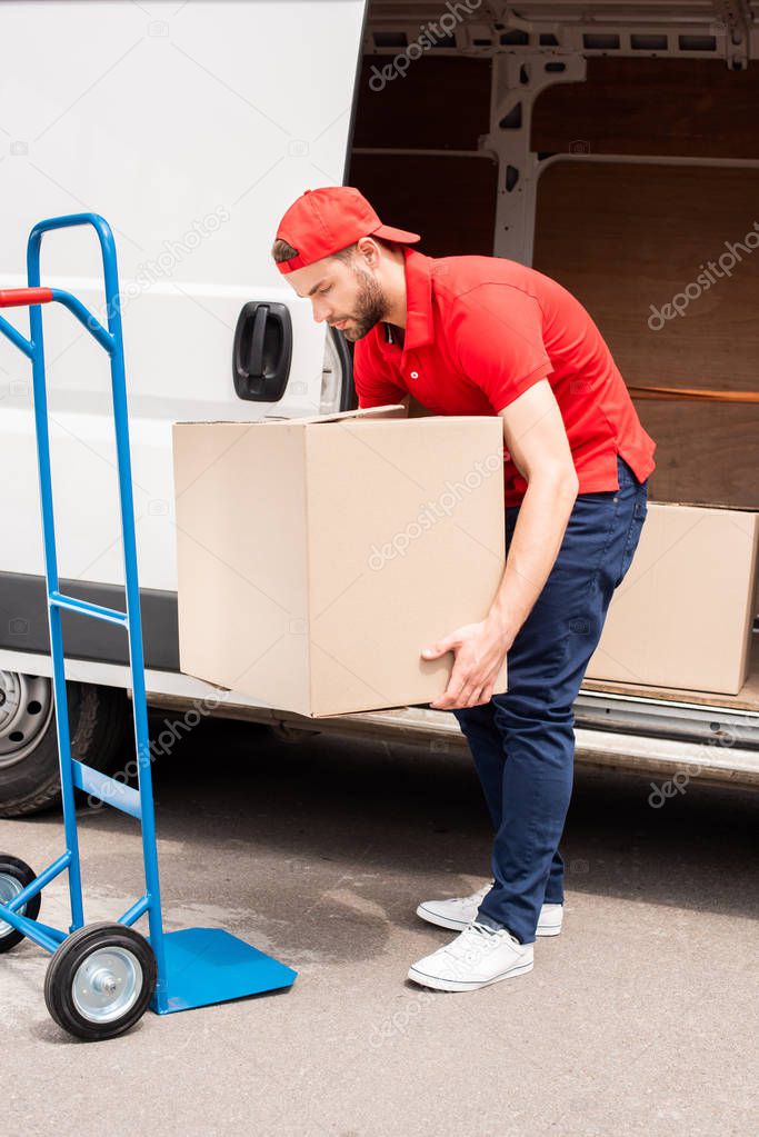young delivery man discharging cardboard boxes from van