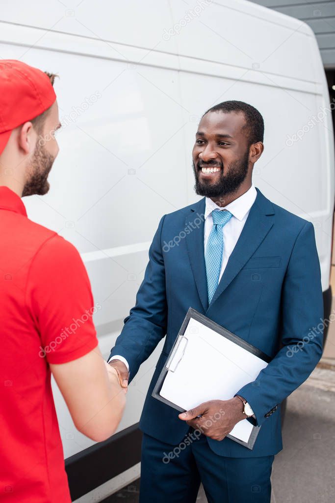 smiling delivery man and african american businessman shaking hands
