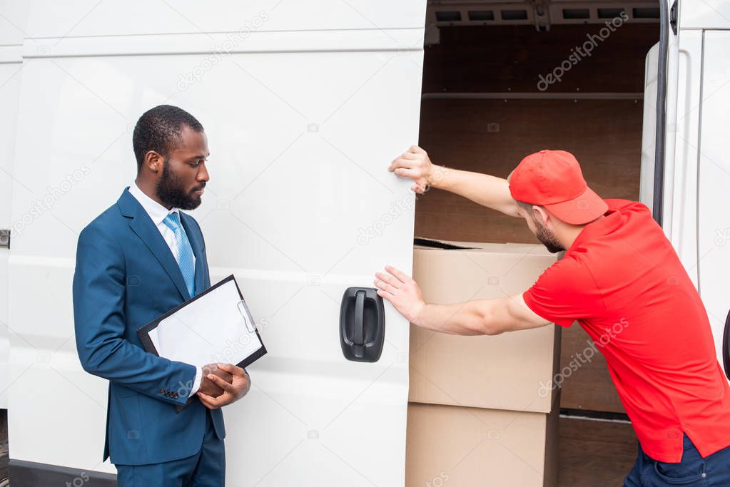 african american businessman with notepad looking at caucasian delivery man closing van with cargo