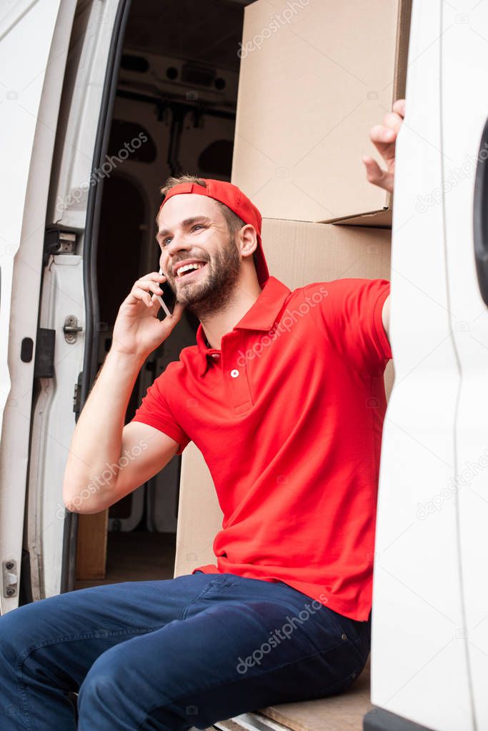 smiling delivery man in red uniform talking on smartphone while resting in van