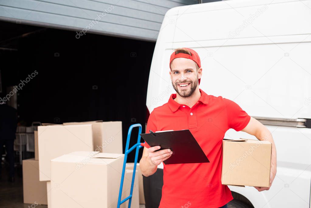 portrait of young smiling delivery man with cardboard box and notepad