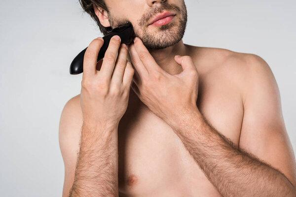partial view of shirtless man with electric clipper shaving beard isolated on grey