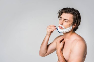 side view of shirtless man with foam on face shaving beard isolated on grey clipart