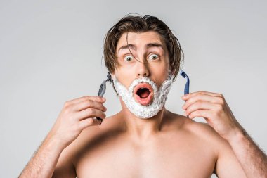 portrait of shocked man with shaving foam on face holding razors isolated on grey clipart