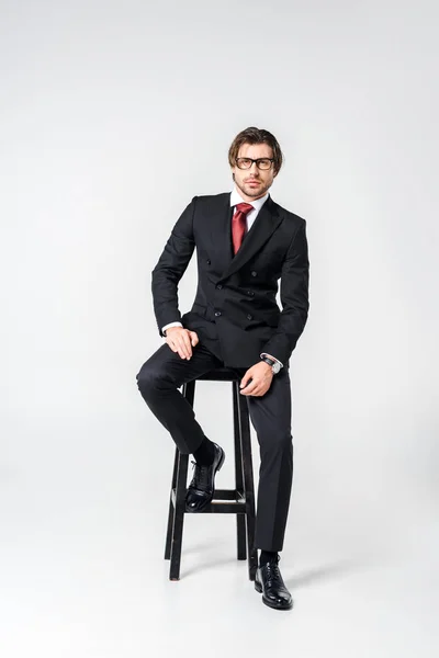 Şık Takım Elbise Gözlük Gri Zemin Sandalyede Oturan Genç Işadamı — Stok fotoğraf