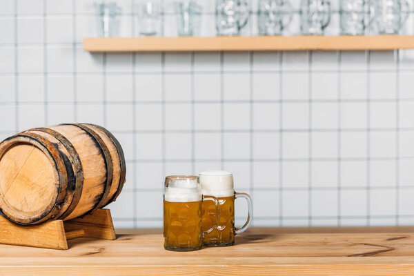 selective focus of beer barrel and two mugs with light beer at bar counter 