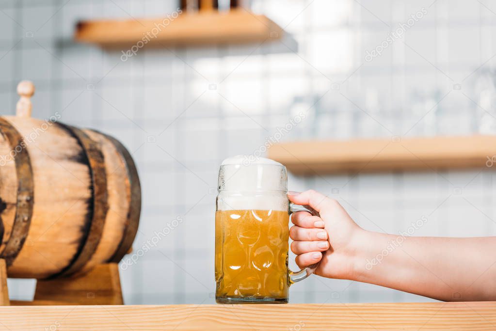 cropped image of female bartender putting mug of light beer with foam on bar counter with beer barrel 