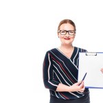 Smiling businesswoman pointing by pen at empty clipboard isolated on white background