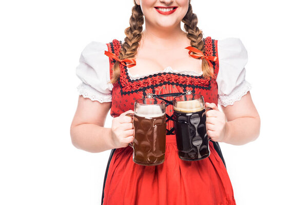partial view of oktoberfest waitress in traditional bavarian dress holding mugs with light and dark beer isolated on white background