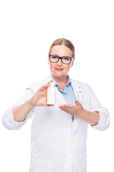 attractive female doctor in eyeglasses pointing at pill bottle isolated on white background 