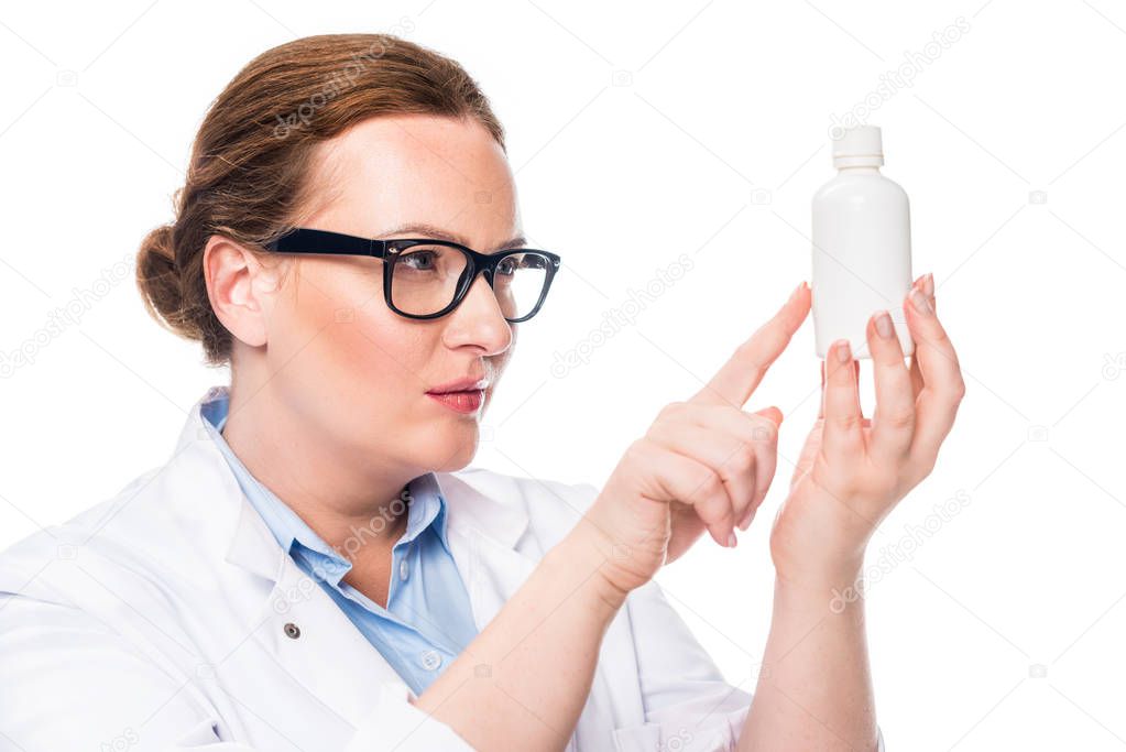 confident female doctor in eyeglasses pointing at pill bottle isolated on white background 