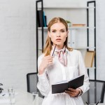 Attractive young businesswoman with notebook leaning back at workplace at modern office