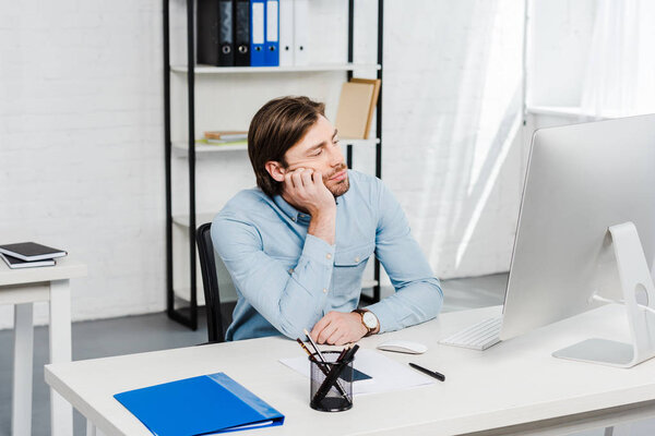 скучающий молодой бизнесмен смотрит на монитор компьютера в офисе
