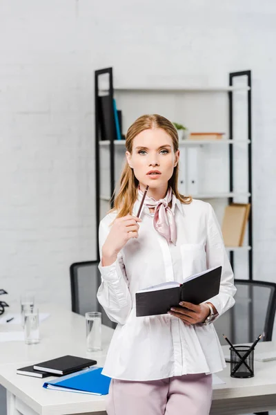 Pengusaha wanita muda yang menarik dengan buku catatan bersandar kembali di tempat kerja di kantor modern — Stok Gambar Pengusaha Wanita Muda Yang Menarik Dengan Buku Catatan Bersandar Kembali Stok Gambar