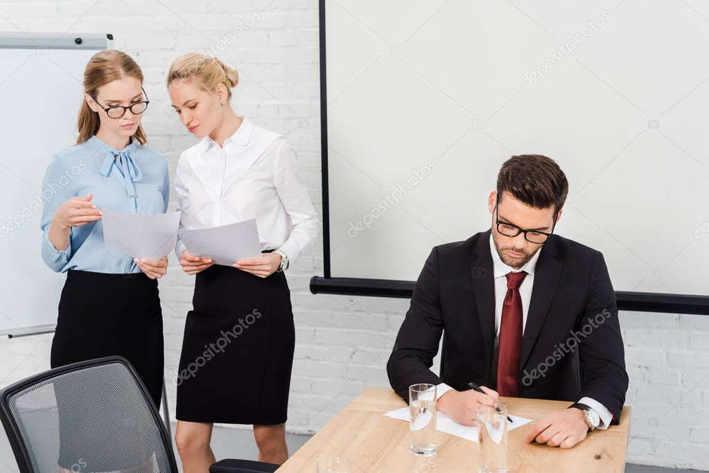 young businesswomen discussing papers while boss writing document at modern office